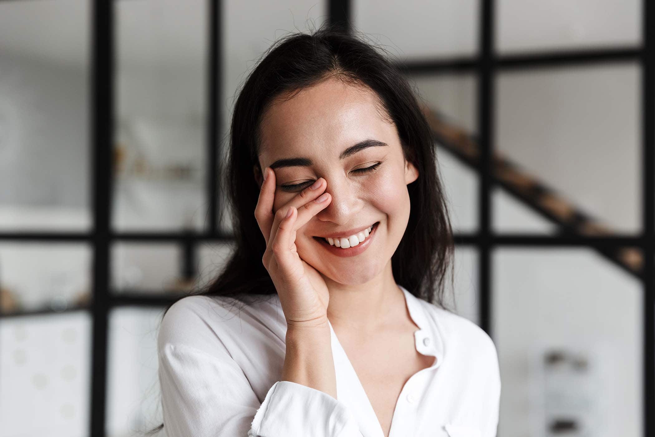 Lächelnde Frau hält eine Hand vor ihr Gesicht.